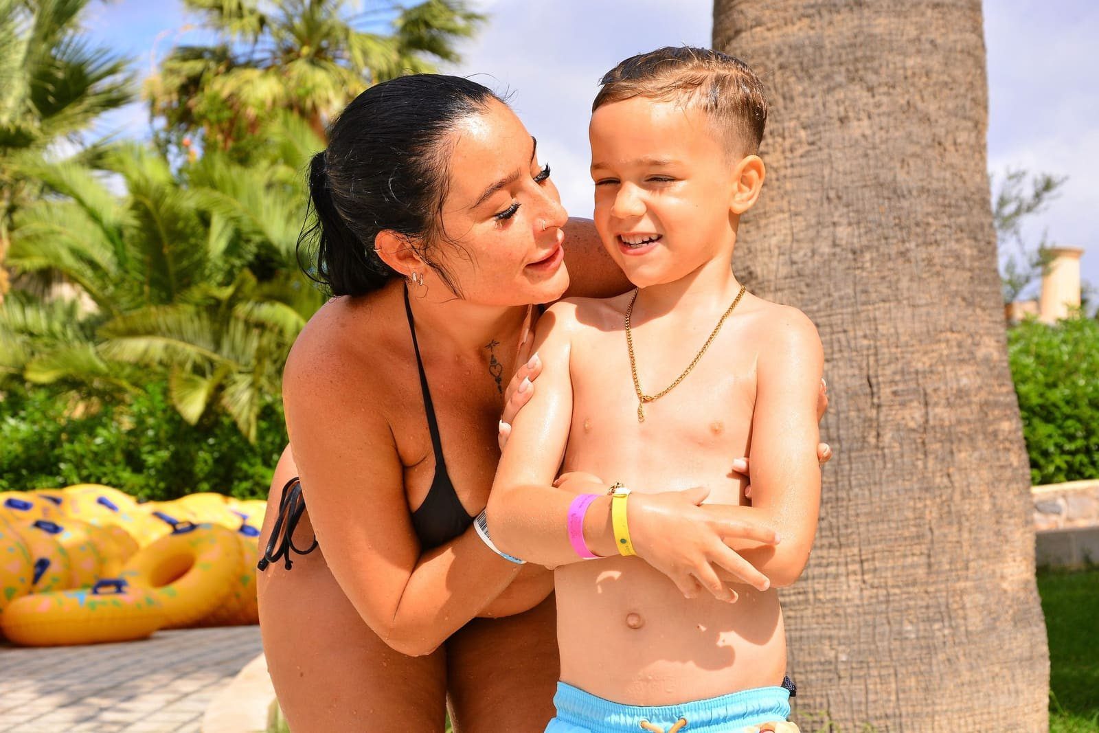 A mother hugs her laughing son by the pool
